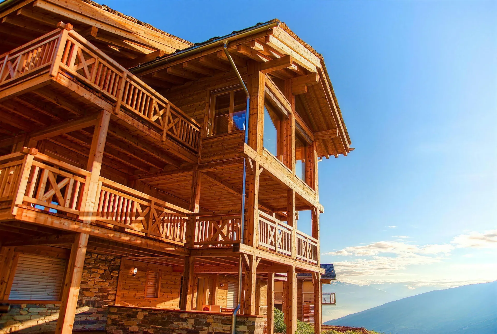 The chalet in summer: wooden balconies in the sun above the valley